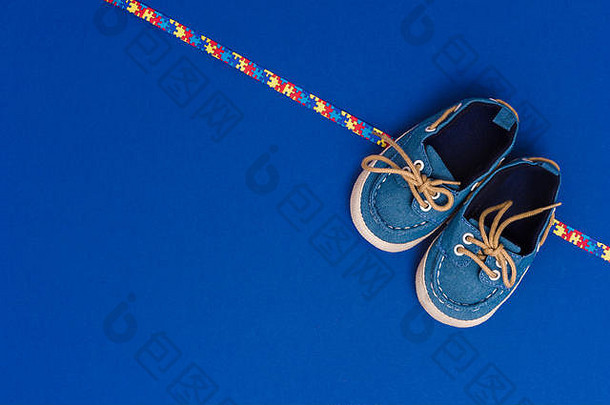 世界自闭症意识日，心理保健概念，蓝色婴儿鞋和缎带拼图图案。在蓝色背景上