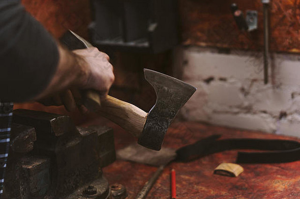 那个人在木工车间工作。他用锤子把木柄上的斧头弄直。男人在工作。手工工作。