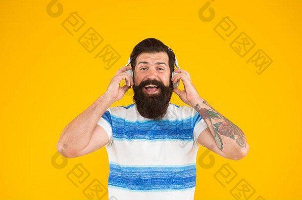 夏季播放列表。暑假音乐。留着胡子、留着长胡子的时髦男人，戴着黄色背景的耳机听歌曲。暑假穿条纹衬衫的家伙。放松的旋律。