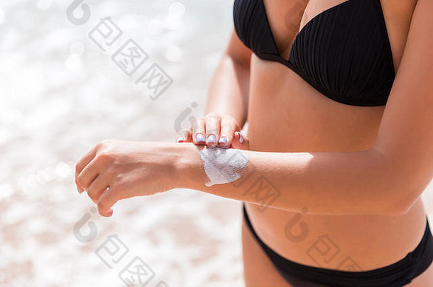 海滩上，一个漂亮的女孩正在手上涂<strong>防晒霜</strong>。