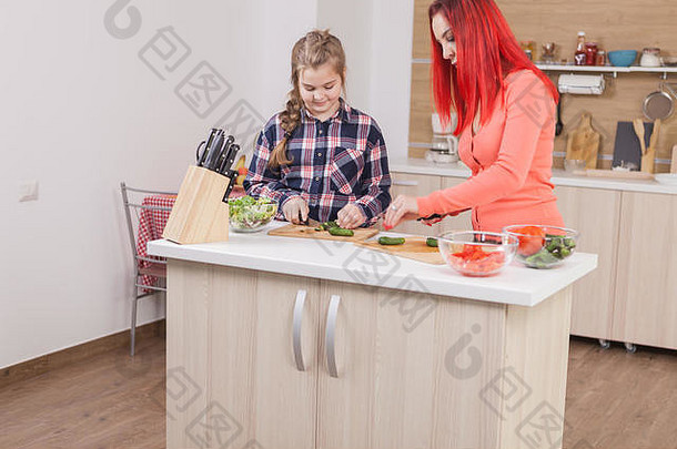 母亲帮女儿切黄瓜做沙拉。美味的蔬菜。
