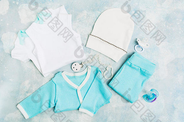 新生儿服装-白色连体衣、蓝色衬衫、蓝色裤子、白色帽子和奶嘴，背景为蓝色纹理。婴儿淋浴概念