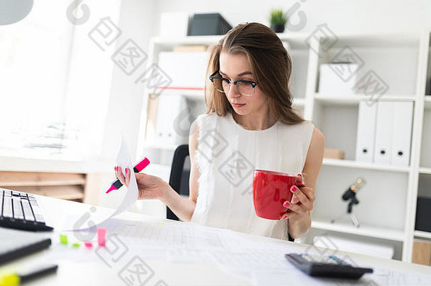 办公室里的一个年轻女孩拿着一个粉红色的马克笔，一个红色的马克杯，文件。