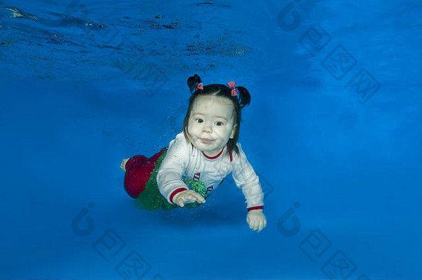 穿着漂亮鲜艳衣服的小女孩在游泳池的水下游泳