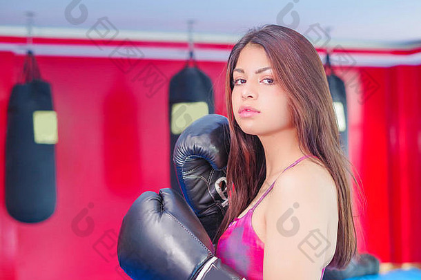 穿着运动手套、留着黑发的漂亮女人，在健身房打拳击。