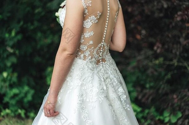 穿着婚纱的新娘。白色婚纱背面蕾丝装饰的特写镜头。户外背景。婚礼日概念。