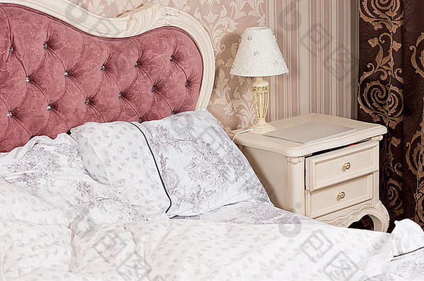 浪漫的豪华卧室内部细节，装饰华丽的软垫粉色床头板，带纽扣和优雅的图案亚麻布。