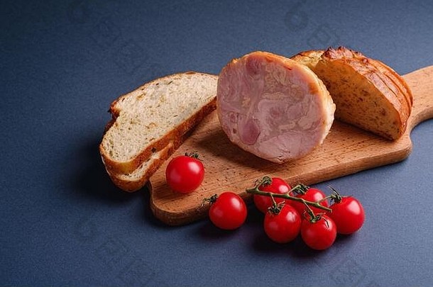 火鸡火腿肉、新鲜樱桃番茄枝和面包片放在木制砧板上，蓝色最小背景，角度视图，复印空间