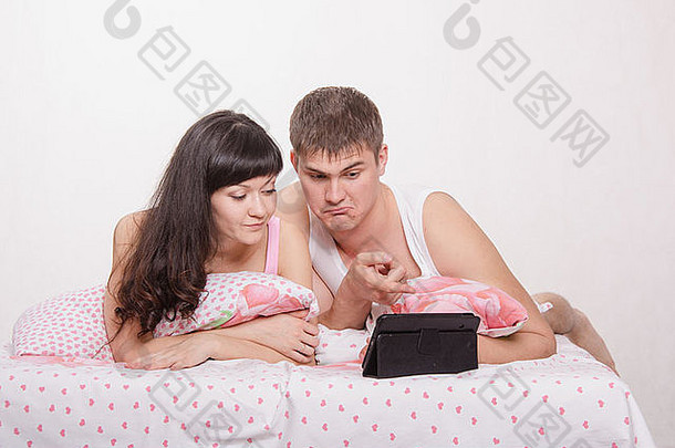 躺在床上用平板电脑看电影的年轻漂亮夫妇