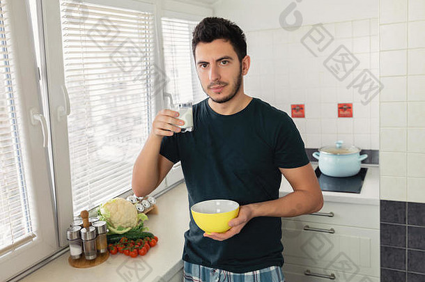 年轻英俊的<strong>男</strong>子正在家里的厨房里吃早餐。那家伙为自己准备了燕麦粥和一杯牛奶作为早餐。