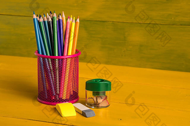 黄色板上金属网格容器中的彩色铅笔。