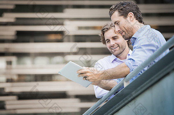 两名男子在<strong>城市</strong>人行道上，看着一台数字平板电脑。