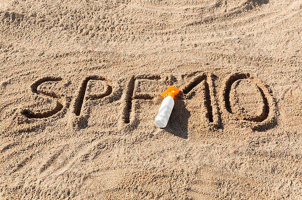 防晒系数十。SPF 10字写在沙子上，白色的瓶子上涂有防晒霜。皮肤护理概念背景。