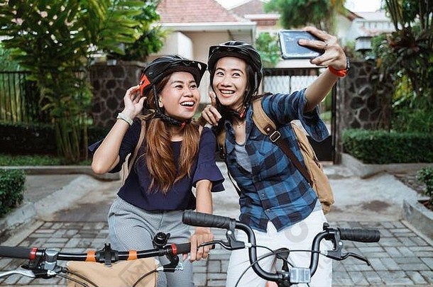 两名亚洲年轻女子戴着头盔，背着照相手机，在去校园前在<strong>折叠自行车</strong>上拍摄视频内容