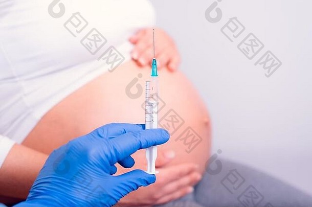 怀孕了女人医学注射手蓝色的手套持有注射器前面怀孕了肚子