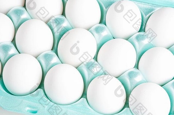 一个明亮的绿色泡沫塑料板条箱的特写镜头，里面装满了白色鸡蛋，背景是白色的。