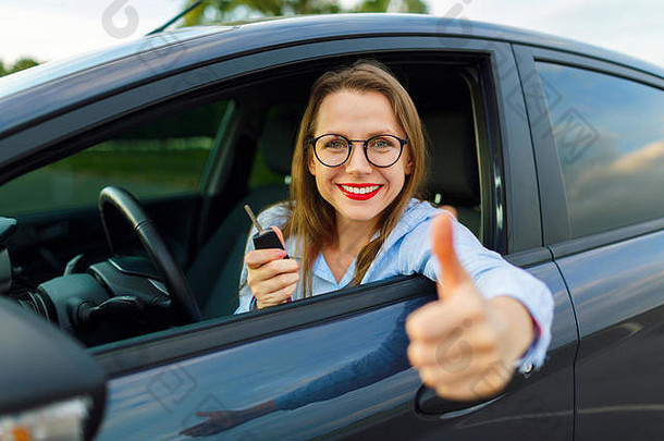 年轻快乐的女人坐在车里竖起大拇指——买二手车或租车的概念