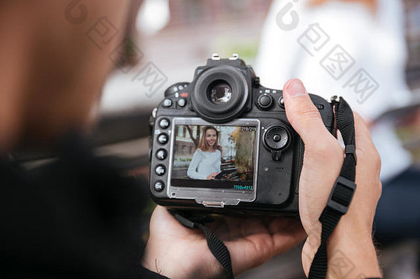 男子摄影师手持专业照相相机，在公园里为美丽的年轻女子拍照