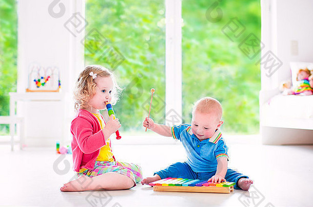 两个孩子——可爱的卷曲蹒跚学步的小女孩和有趣的小男孩，兄弟姐妹用五颜六色的木琴和长笛演奏音乐