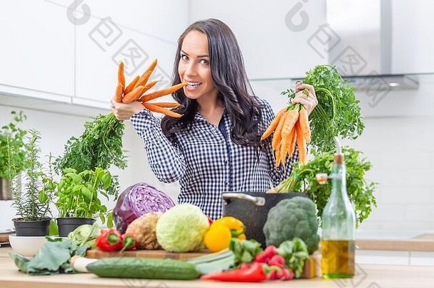 在厨房里，一个顽皮的年轻女子双手捧着新鲜的胡萝卜——节食蔬菜和健康概念。