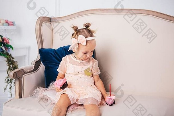 2岁的有趣女孩穿着粉色公主裙坐在家里吃蛋糕。主题是儿童节。儿童天然糖果。糖尿病与疾病