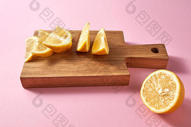 粉红色背景上木板上多汁成熟的有机黄色柠檬片的特写镜头。