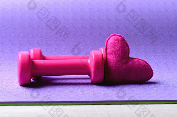 杠铃和粉情符号，特写。粉色塑料制成的哑铃靠近柔软的玩具心，背景为紫色纹理，复制空间。热爱运动和<strong>健身</strong>器材。健康生活方式理念。