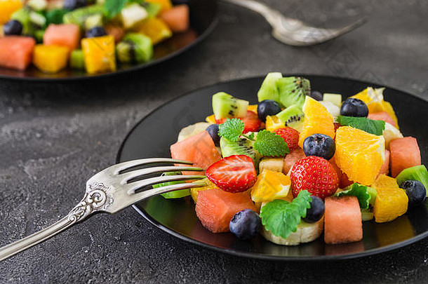 健康的新鲜的水果沙拉黑色的板黑暗背景美味的夏天餐草莓蓝莓橙子猕猴桃香蕉西瓜乳香