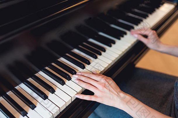 在黑钢琴上演奏的女孩。只有手是看得见的。