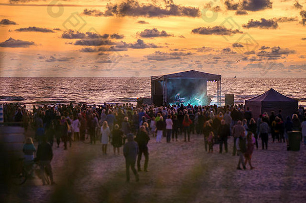 一群面目全非的人。日落时分在海边举行的浪漫音乐会。人们聚集在一起庆祝夏天的结束