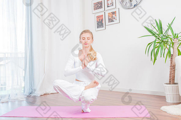 美女在家里瑜伽垫上练习瑜伽，女孩做半莲花脚趾平衡练习，蹲着坐着