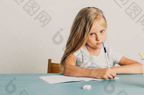 金发女孩坐在桌子旁，在笔记本上写字