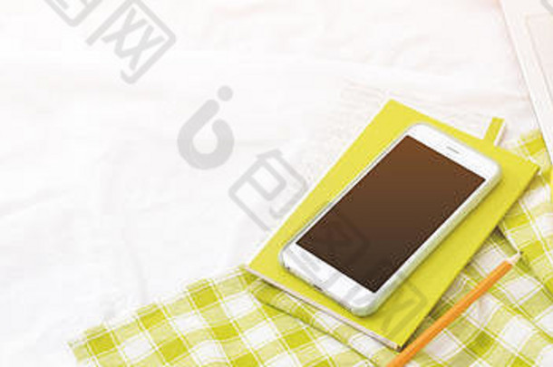 长长的横幅平放着电话，一杯黄色的茶，笔记本电脑和鲜花，放在白色的毯子上，还有绿色的餐巾