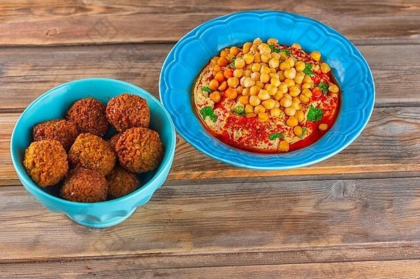 在一个盘子里放一个法拉费丸子，在木桌上的盘子里放一个鹰嘴豆泥、鹰嘴豆、塔希尼和橄榄油、胡椒、香料。传统的中东<strong>健康</strong>素食食品。