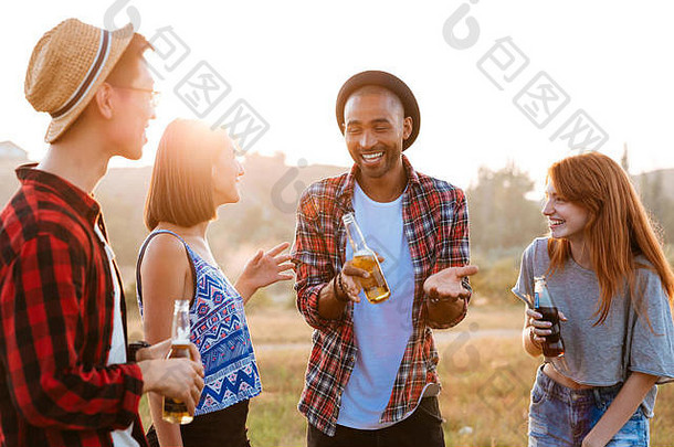 多民族的快乐年轻人，喝着啤酒和苏打水，在户外谈笑风生