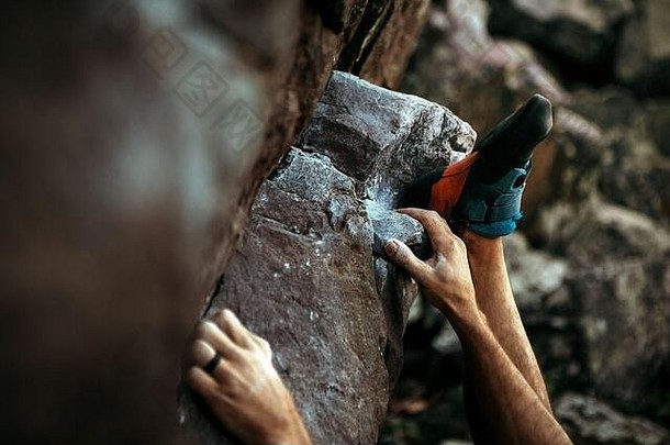 一个攀岩者手上戴着黑色结婚戒指和<strong>登山鞋</strong>的特写镜头，他用力爬上一块岩石巨石
