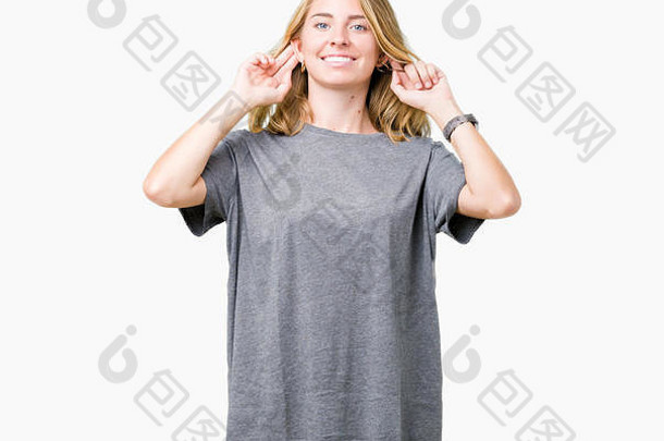 美丽的年轻女子穿着超大号休闲t恤，在孤立的背景下微笑着用手指拉耳朵，滑稽的手势。试听问题