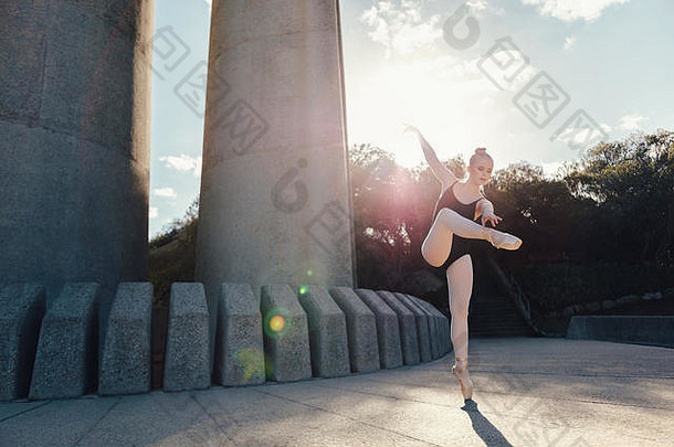芭蕾舞演员在户外练习舞蹈动作，背景是阳光。穿着尖头鞋单脚趾站立练习舞步的女舞者。