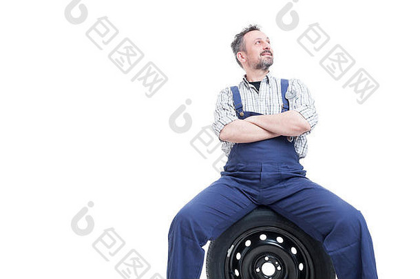 英俊的机械师自信地站着，双臂交叉放在轮胎上，孤立地看着白色的复印区
