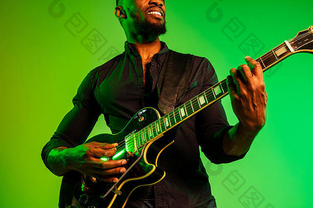 年轻的非洲裔美国音乐家，在渐变的绿黄色背景上像摇滚明星一样弹奏吉他。音乐的概念，爱好，节日，露天。快乐迷人的家伙即兴表演，唱歌。