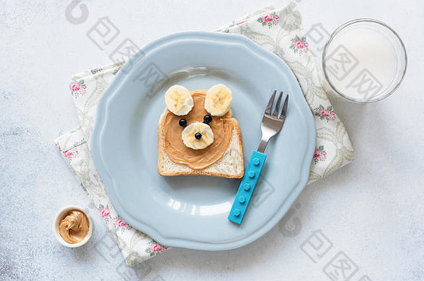 蓝色盘子上的香蕉花生酱吐司，<strong>儿童餐</strong>。可爱有趣的熊形动物吐司，配坚果黄油和香蕉。孩子们的学校午餐。治愈