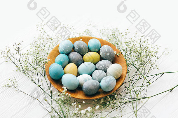 复活节快乐。在白色木质背景上的木制板上，装饰有春天花朵的时尚复活节彩蛋。用耶洛天然染料绘制的现代复活节彩蛋