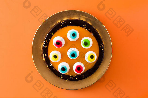 万圣节蛋糕，橙色背景上有糖果眼装饰。顶视图。
