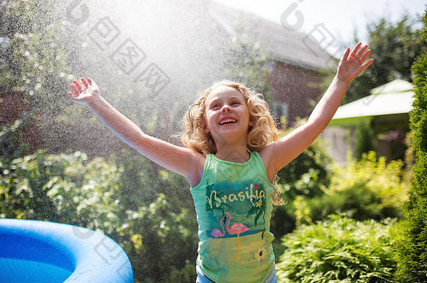 学龄前可爱的女孩在玩花园洒水器。夏季，后院的户外水上娱乐。