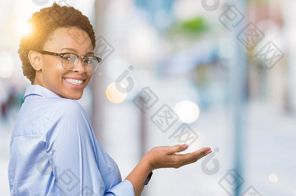 年轻美丽的非裔美国女商人，在孤立的背景下，用手和张开的手掌指向侧面，展示了广告中的微笑和幸福