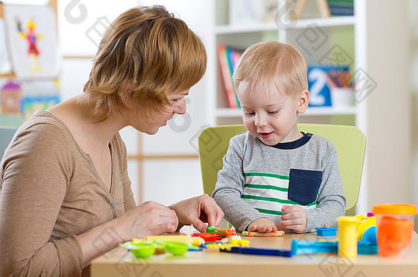 育儿室里，一个女人和一个小男孩在桌子旁玩橡皮泥
