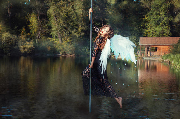 长着天使翅膀的女孩在杆子上跳舞。竿子舞在河中央。