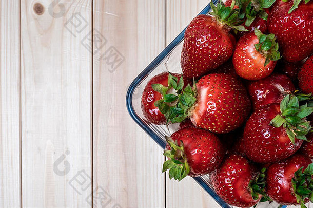 在一张轻薄的木桌上放着一个方形的玻璃碗和草莓。大草莓。