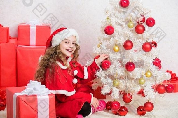 珍爱的节日活动。孩子们喜欢家庭传统。平安夜概念。参加圣诞节庆祝活动。女孩微笑着可爱的圣诞老人坐在圣诞树旁。孩子在装饰圣诞树。