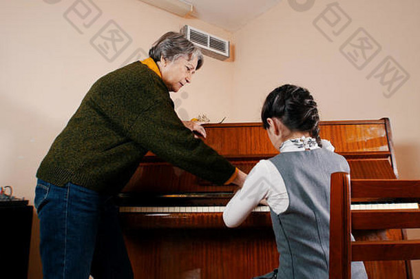 一个小女孩在音乐课上弹钢琴。帮助她的老师